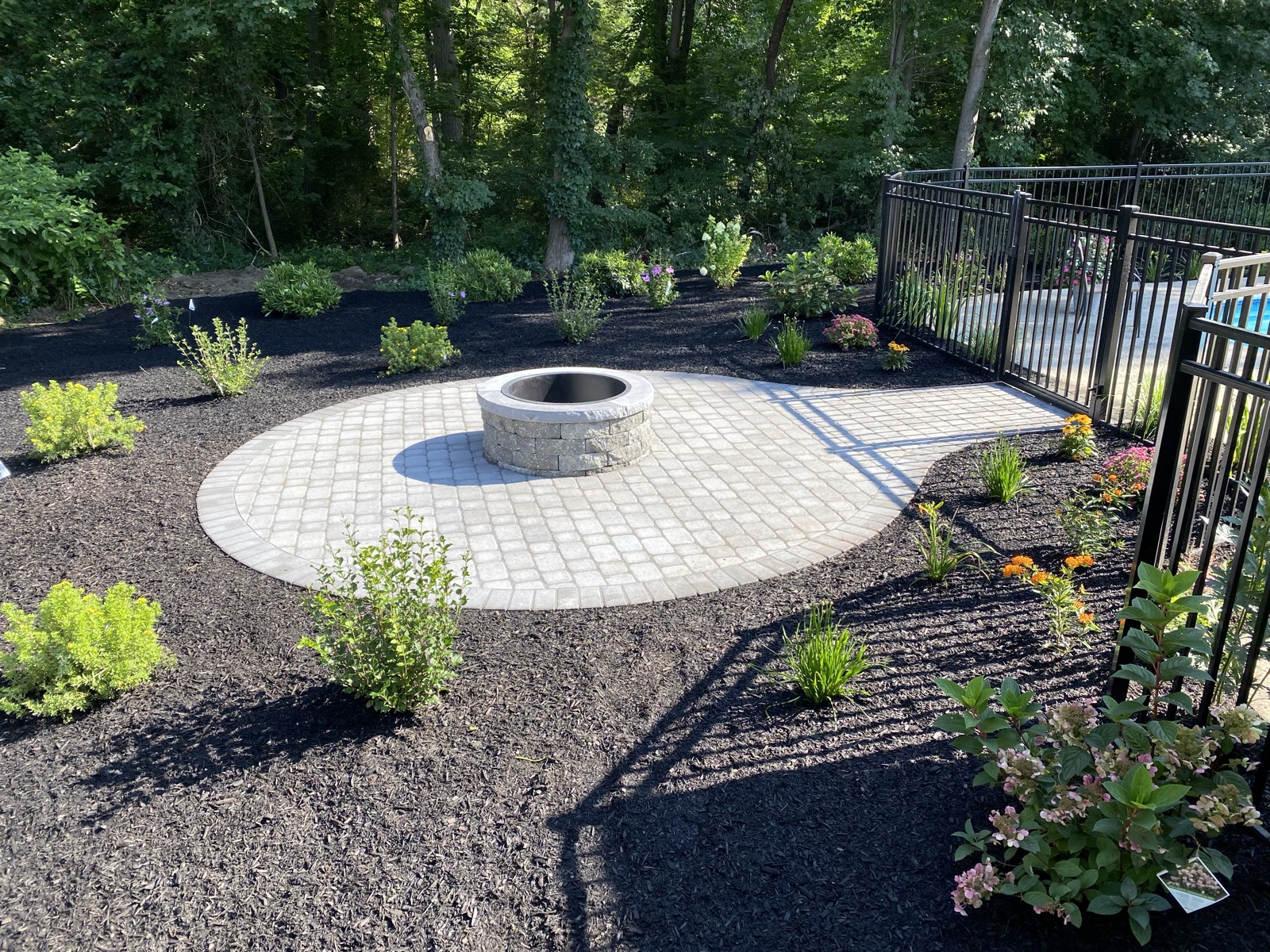 Circular paver patio with a stone fire pit bordered by fresh plantings in a residential backyard